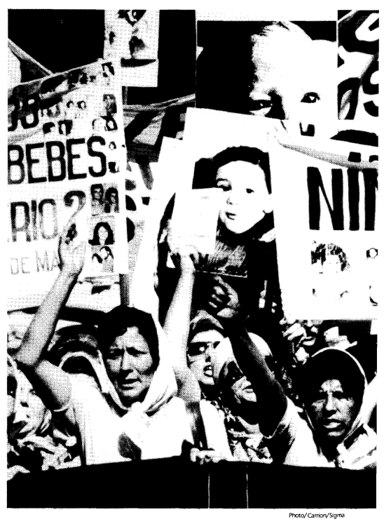 A group of protestors with scarves around their hair hold up signs with images of children and parts of words including "Bebes ... Rio?"